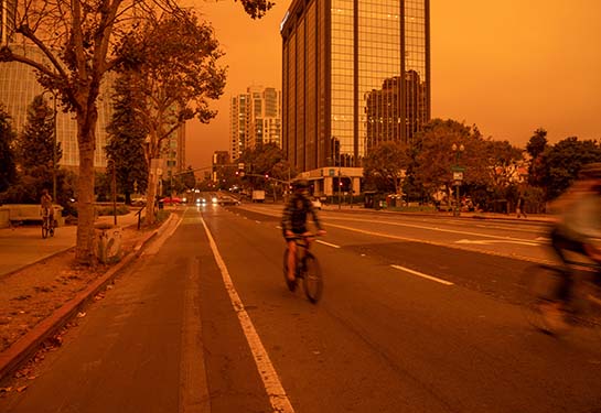 A bicyclist is shown biking on a street in Oakland, California, on a very smoky day.   